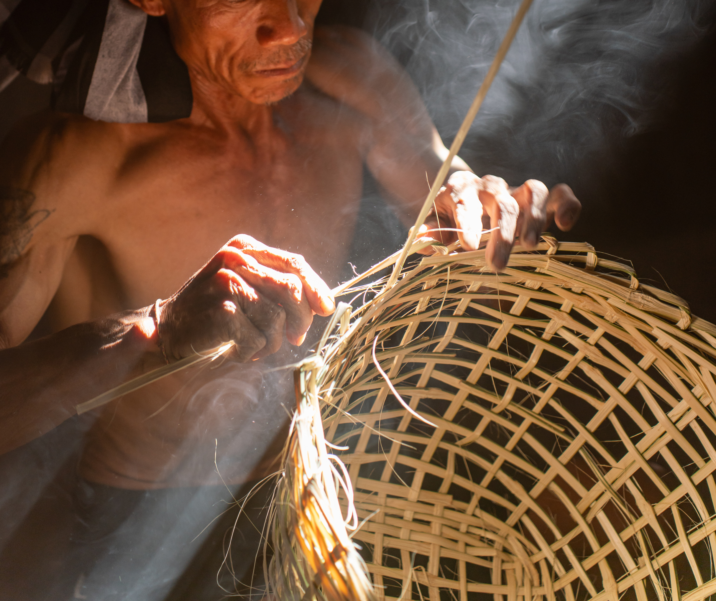 Asian village lifestyle, moment a local male adult uncle basket weaver maker making bamboo basket and hat in a dry grass built room, very beautiful scenic view